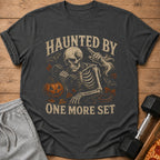 Dark grey t-shirt with skeleton lifting weights and "HAUNTED BY ONE MORE SET" text.