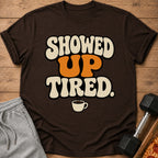 Brown t-shirt with text "SHOWED UP TIRED." and a coffee cup graphic.