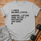 Gray t-shirt with text: "> CHECK BALANCE_STATUS... WARNING: LIFTING MODE ACTIVE / MOTIVATION SUB-ZERO"