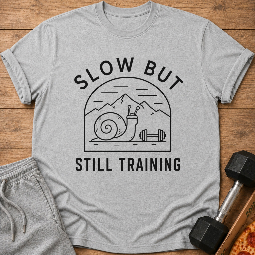 Gray t-shirt with a line drawing of a snail with a dumbbell and mountains, text reads "SLOW BUT STILL TRAINING".