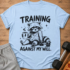 Light blue t-shirt with graphic of tired raccoon drinking coffee and text "TRAINING AGAINST MY WILL."