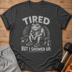 Dark t-shirt with distressed graphic of a tired frog on a bench with weights and text "TIRED BUT I SHOWED UP."