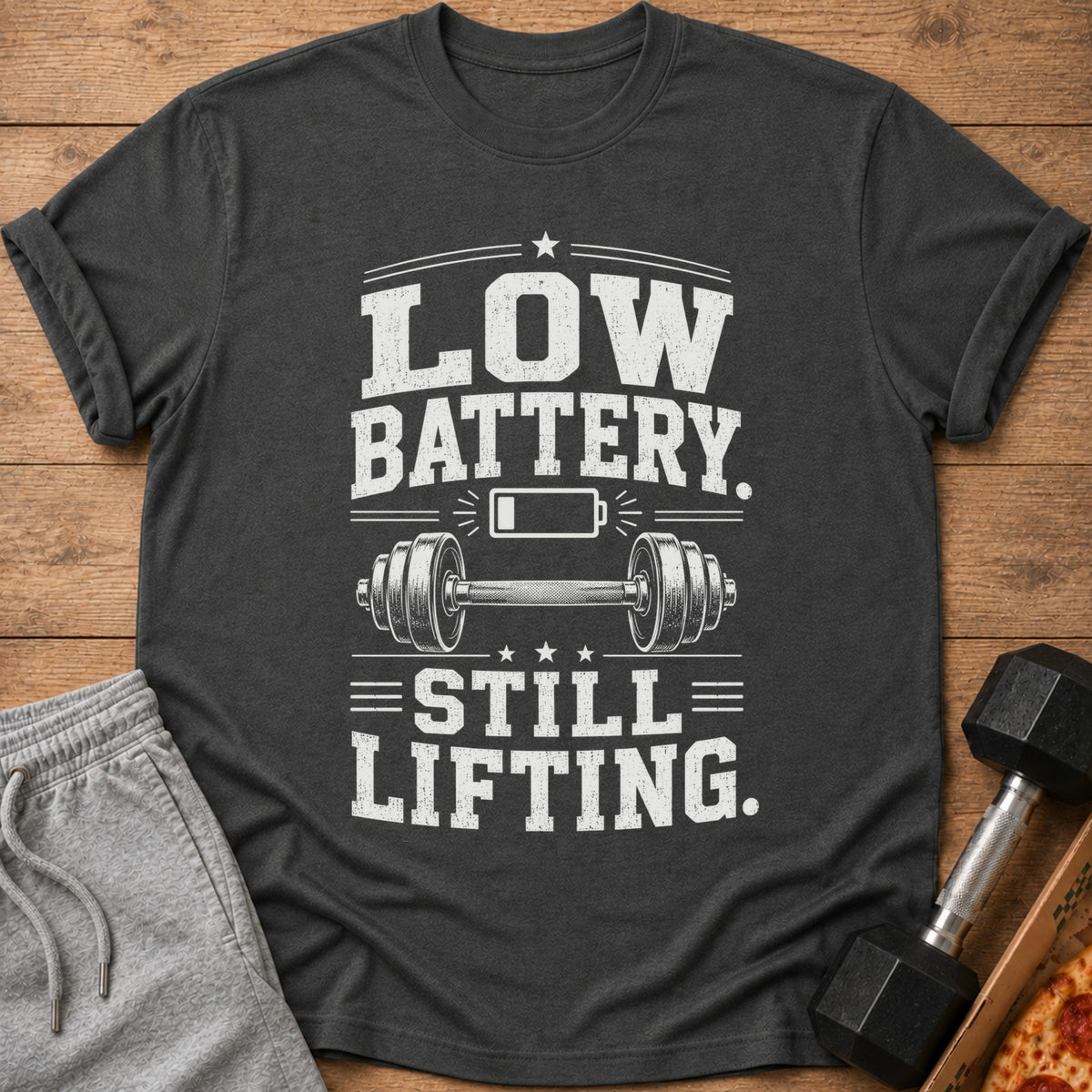 Dark gray t-shirt with "LOW BATTERY. STILL LIFTING." text and dumbbell graphic.