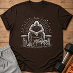 Brown t-shirt with a white graphic of a person in a hoodie sitting on a bench with gym bag.