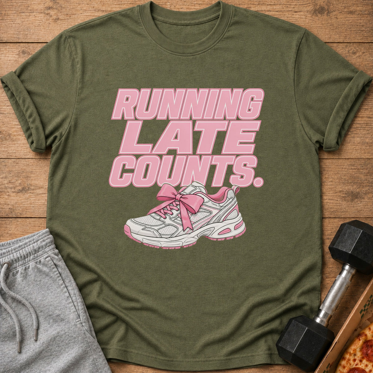 Olive green t-shirt with pink text "RUNNING LATE COUNTS." and a pink bow on a running shoe.