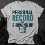 Light gray t-shirt with "Personal Record In Showing Up" text and workout icons.