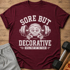 Maroon t-shirt with a cartoon character lifting weights and text "Sore But Decorative".