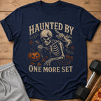 Skeleton lifting weights with text "Haunted By One More Set" and Halloween graphics.