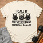 Cream t-shirt with "I Call It Strength Training But Mostly It's Emotional Damage" text and cartoon kettlebells.