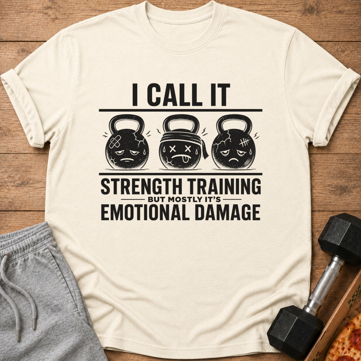 Cream t-shirt with "I Call It Strength Training But Mostly It's Emotional Damage" text and cartoon kettlebells.