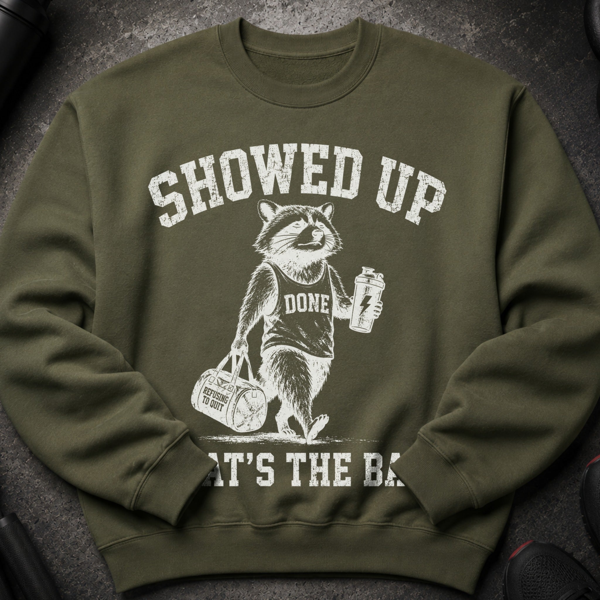 Green sweatshirt with distressed graphic of a raccoon holding a gym bag and shaker.