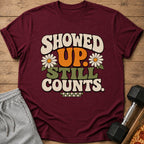 Maroon t-shirt with retro text "SHOWED UP. STILL COUNTS." and daisies.