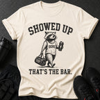 Graphic tee with raccoon holding gym bag and shaker. Text reads "SHOWED UP DONE THAT'S THE BAR."