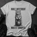 Gray t-shirt with a cat holding a kettlebell and text "BUILT DIFFERENT MOSTLY ANNOYED."