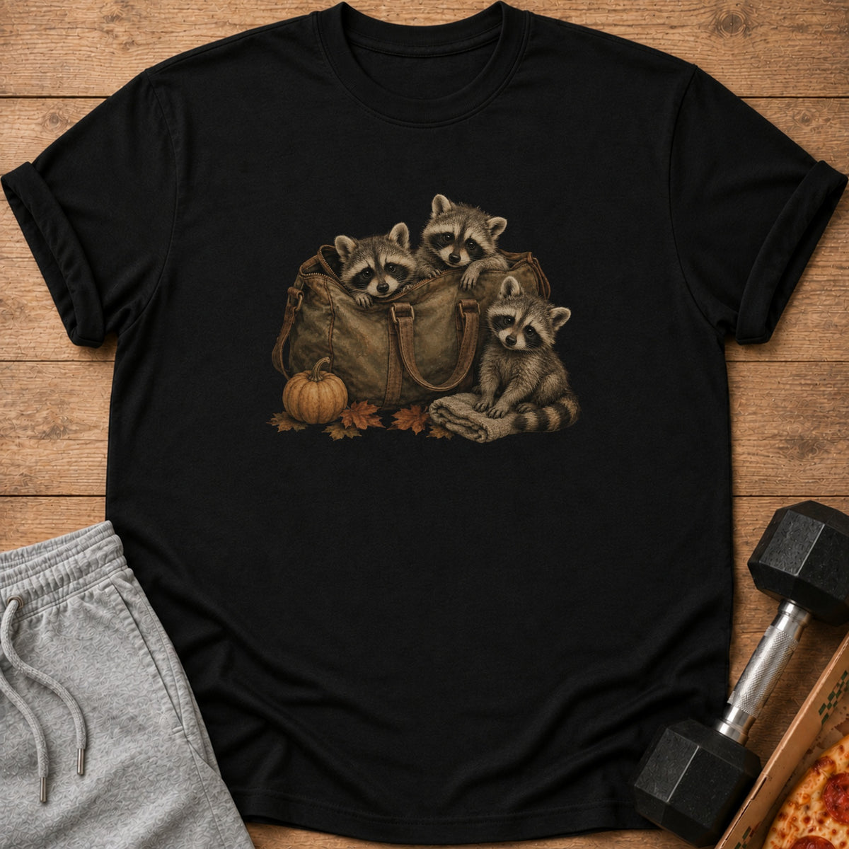 Three raccoons peek out of a duffel bag with a pumpkin and leaves.