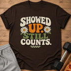 Brown t-shirt with "SHOWED UP. STILL COUNTS." text, daisies, and checkered pattern.