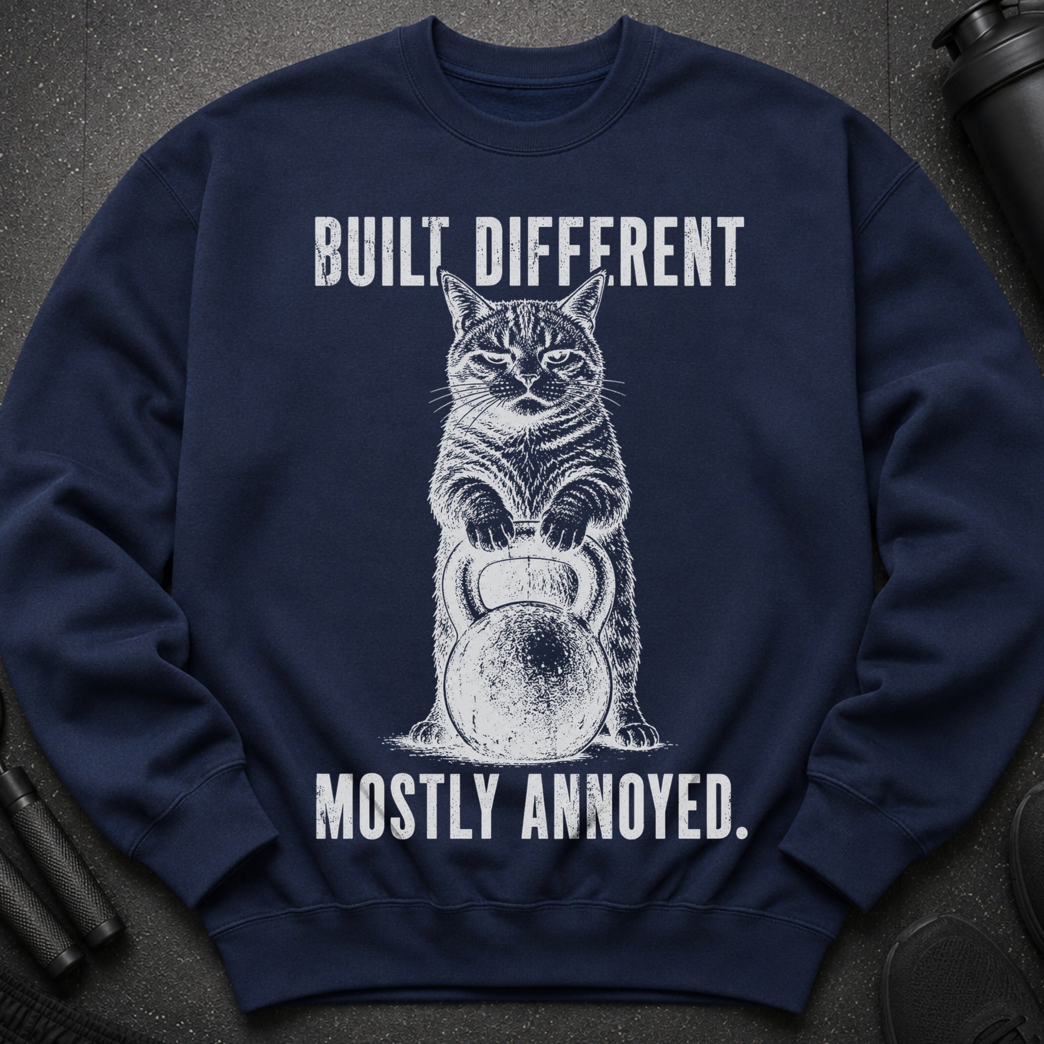 Navy sweatshirt with a cat holding a kettlebell and text "BUILT DIFFERENT MOSTLY ANNOYED."