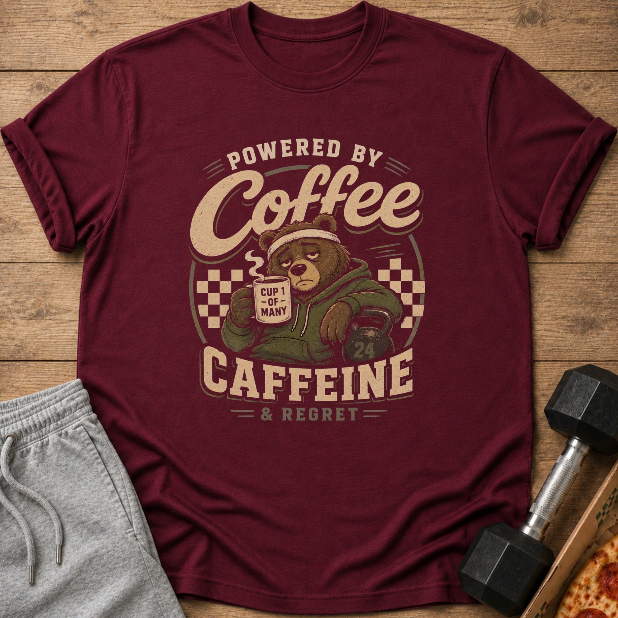 Maroon t-shirt graphic with a tired bear holding coffee that says "CUP 1 - OF - MANY".