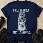 Navy tee with cat holding kettlebell, text "BUILT DIFFERENT MOSTLY ANNOYED."