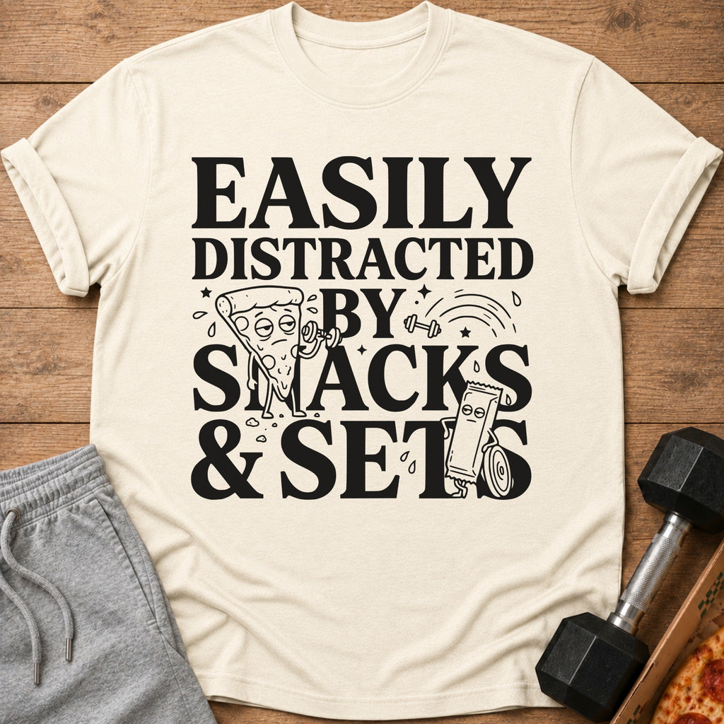 Cream t-shirt with black text "Easily Distracted By Snacks & Sets" and cartoon images.