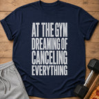 Navy t-shirt with white text reading "AT THE GYM DREAMING OF CANCELING EVERYTHING".