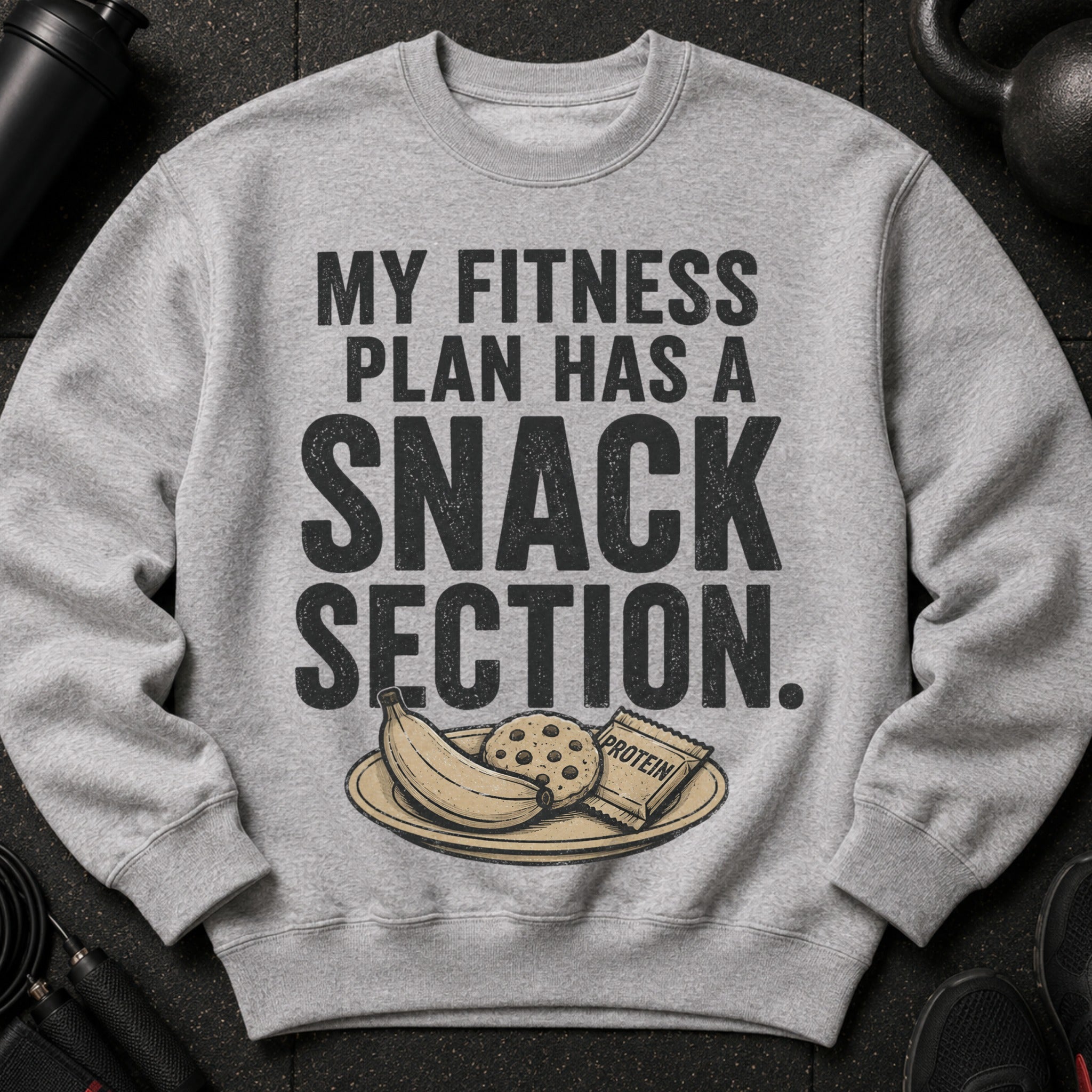 Grey sweatshirt with text "MY FITNESS PLAN HAS A SNACK SECTION" and a plate of banana, cookie, and protein bar.