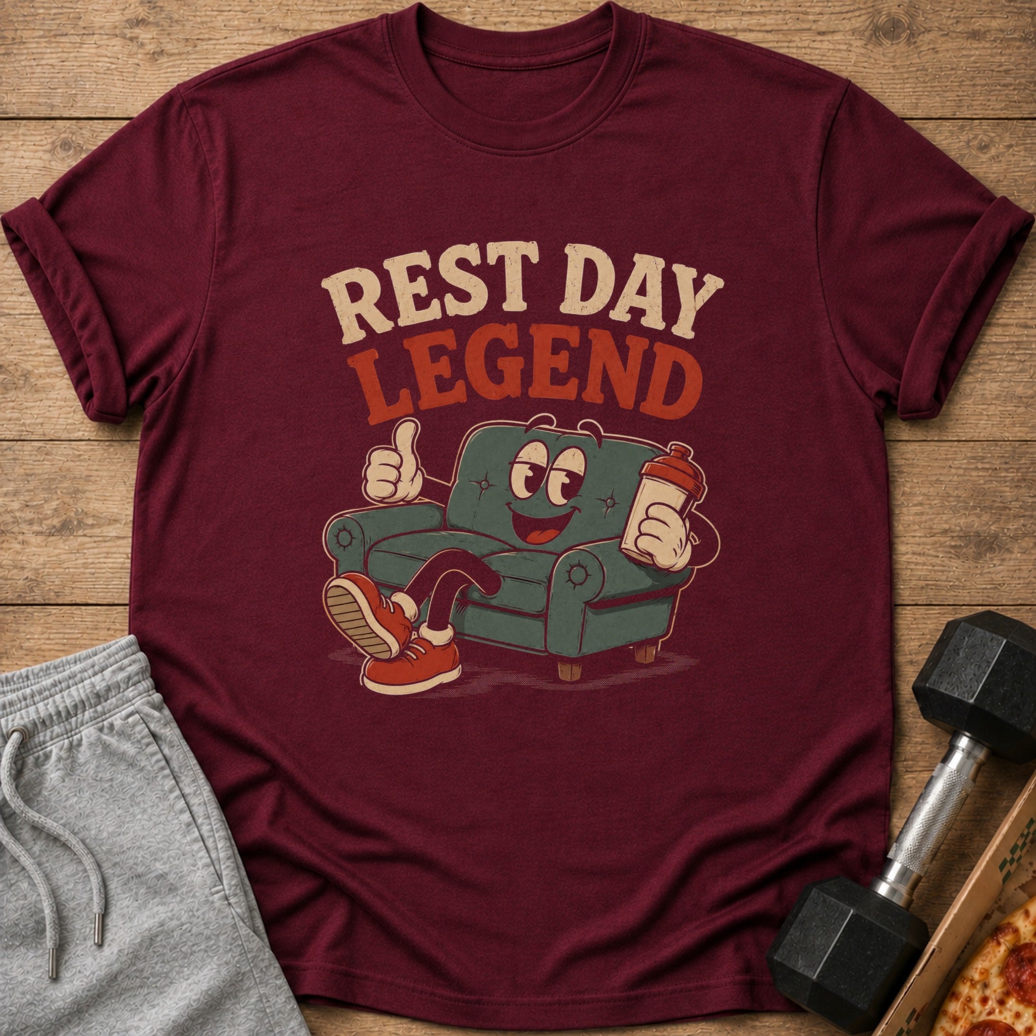 Maroon t-shirt with "REST DAY LEGEND" text and cartoon sofa holding a shaker bottle.