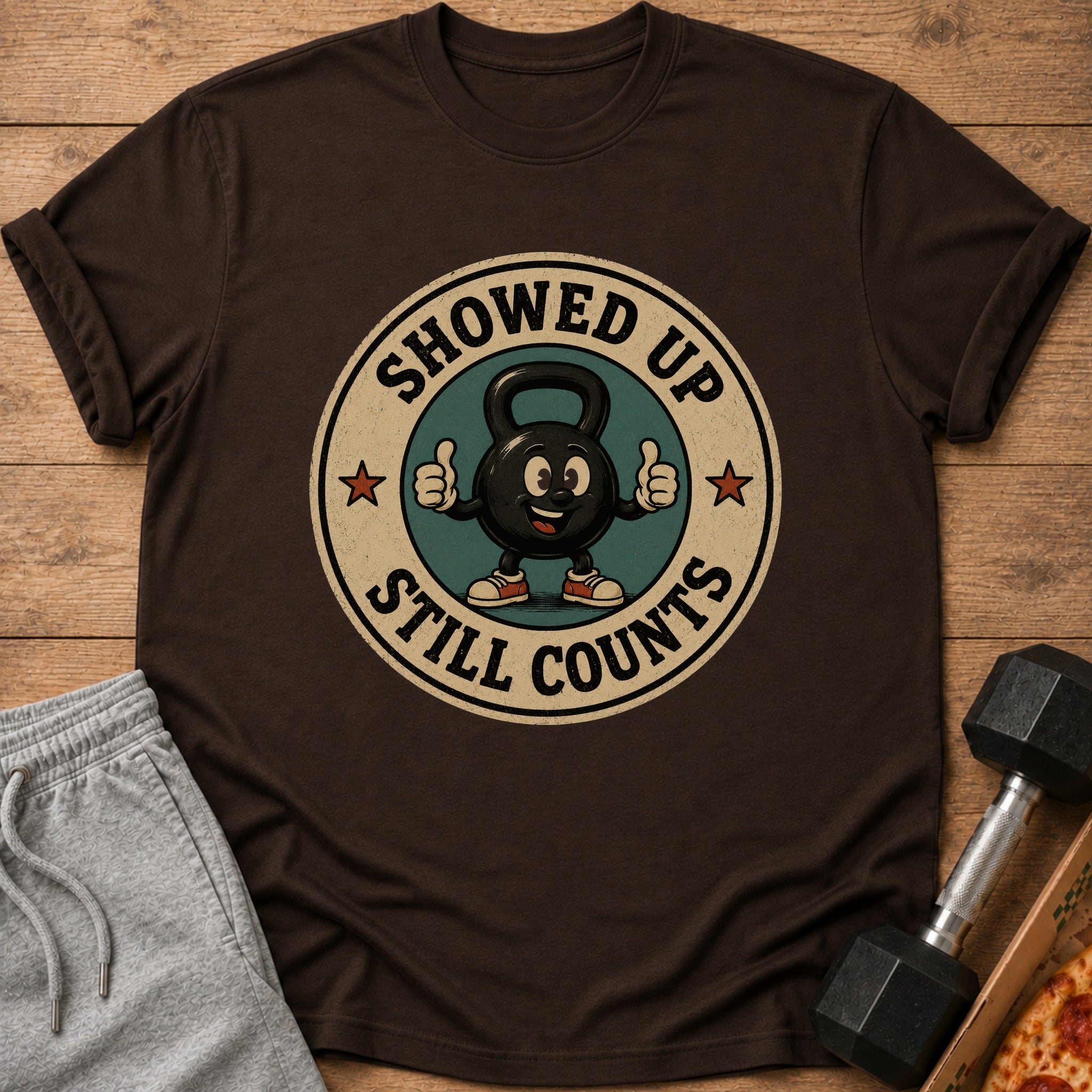 Brown t-shirt with a circular graphic featuring a cartoon kettlebell and text.