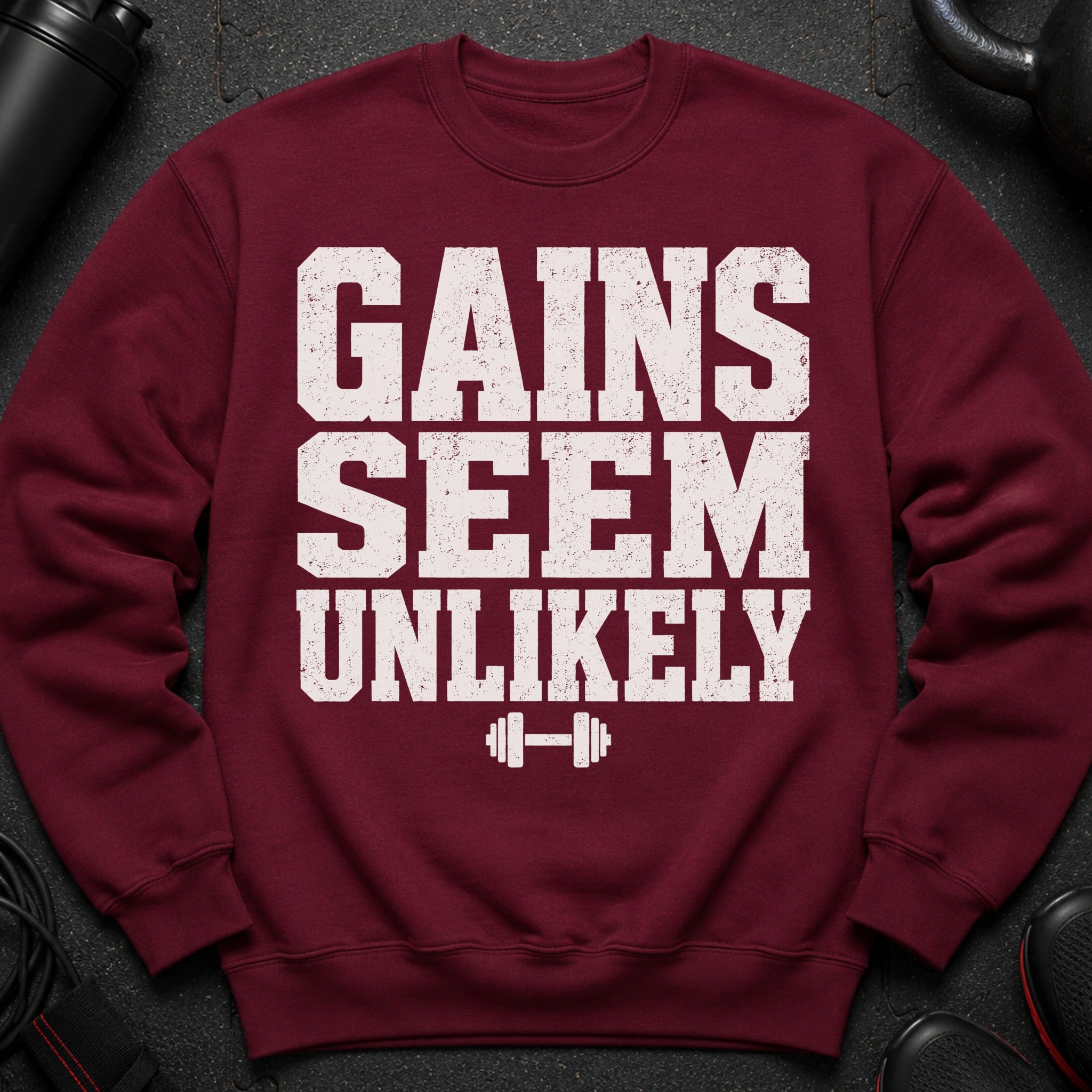 Maroon sweatshirt with white text "Gains Seem Unlikely" and a dumbbell graphic.