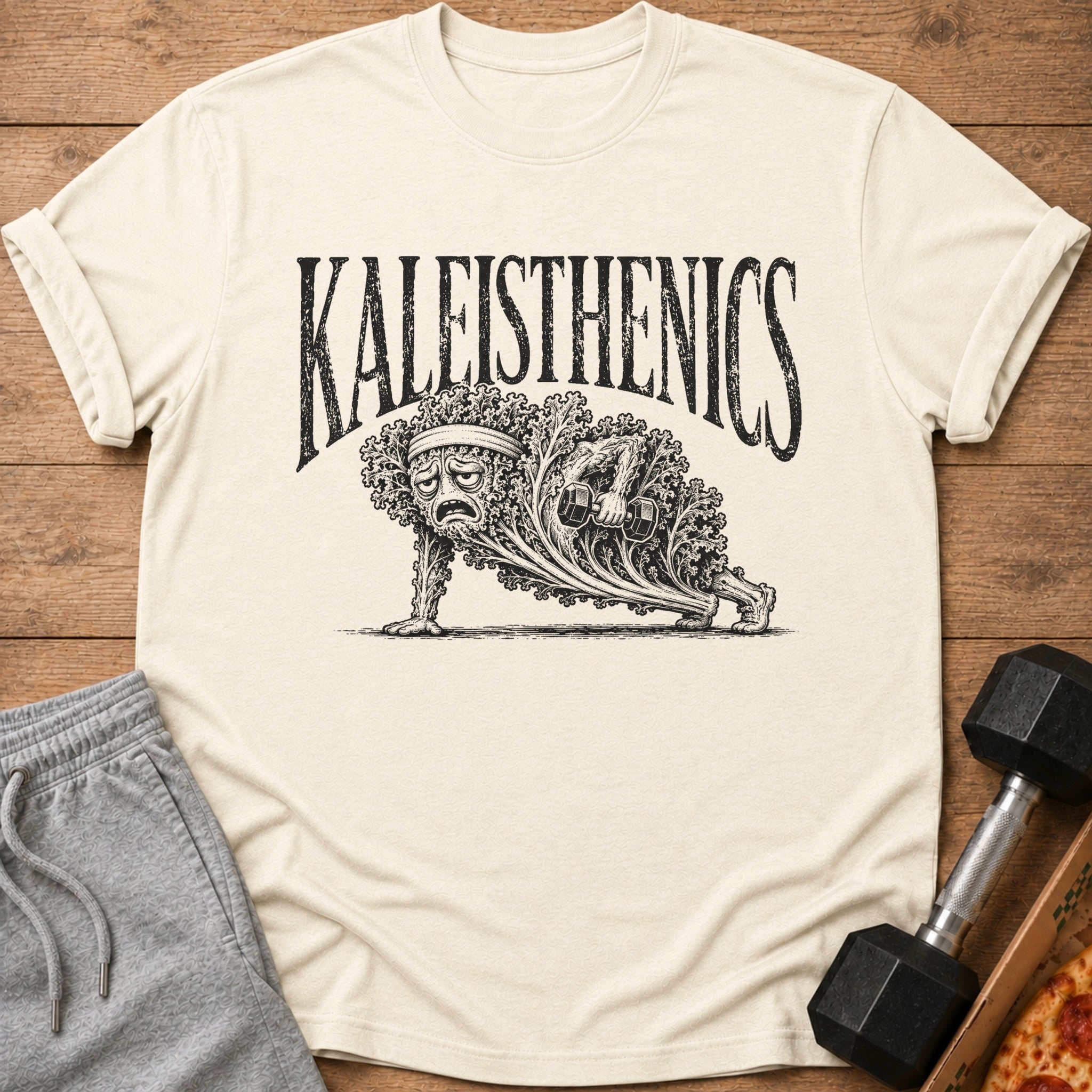 T-shirt with a distressed black graphic of a sad kale character doing a push-up with dumbbells.