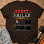 Brown t-shirt with pixel art: "Quest Failed Successfully," a character, treadmill, and game stats.