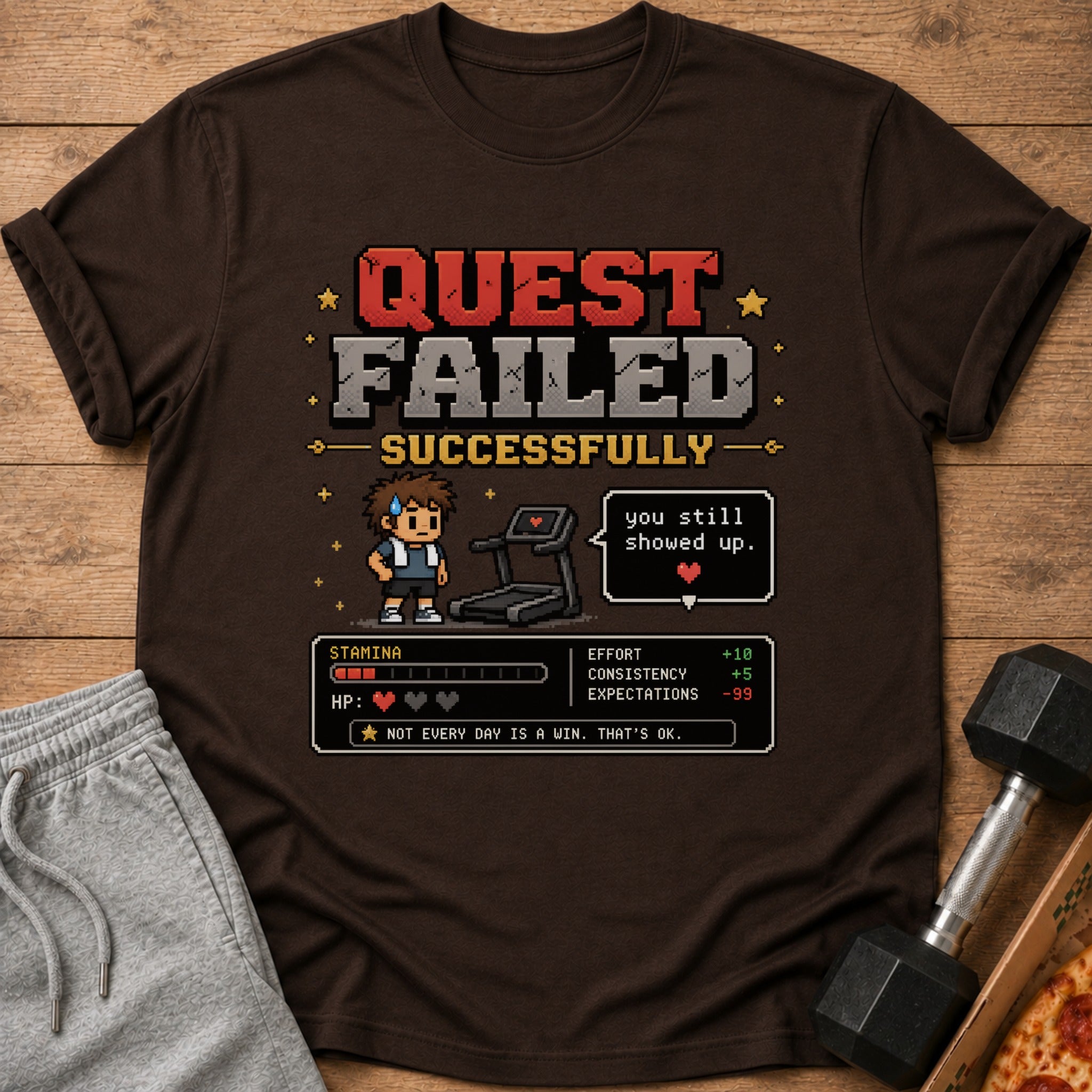 Brown t-shirt with pixel art: "Quest Failed Successfully," a character, treadmill, and game stats.