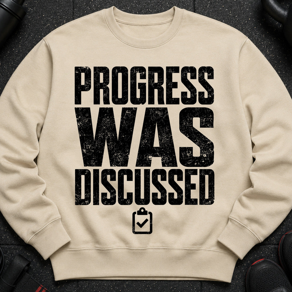 Beige sweatshirt with black text "PROGRESS WAS DISCUSSED" and a clipboard icon.