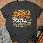 Dark grey t-shirt with vintage style text "SHOWED UP STILL COUNTS" and floral graphics.