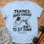 Light blue t-shirt with cartoon man on workout box, "Trained Hard Enough To Sit Down".