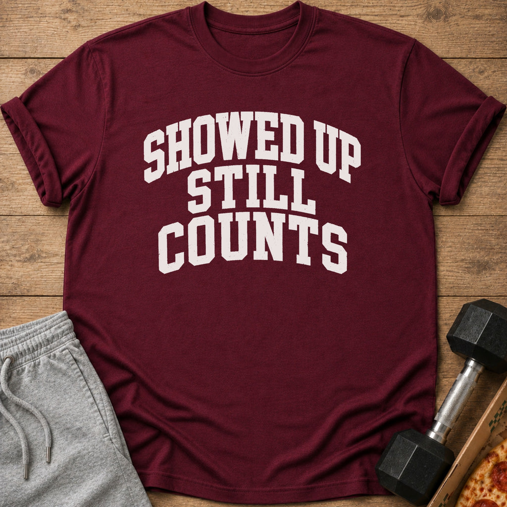Maroon t-shirt with "SHOWED UP STILL COUNTS" text, sweatpants, dumbbell, and pizza.