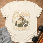 Cream t-shirt with a tired bear holding coffee and text "Powered by Coffee, Caffeine & Regret."