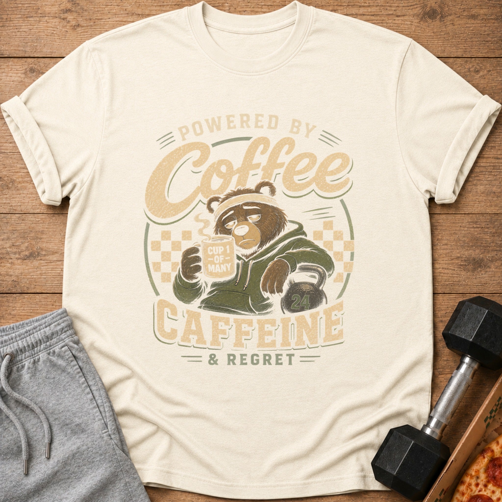 Cream t-shirt with a tired bear holding coffee and text "Powered by Coffee, Caffeine & Regret."
