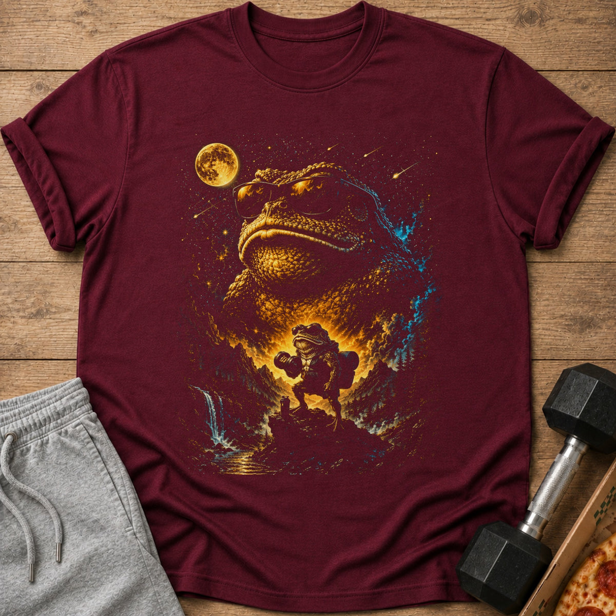 Maroon t-shirt with a surreal print of a giant frog wearing sunglasses and a small frog holding a dumbbell.