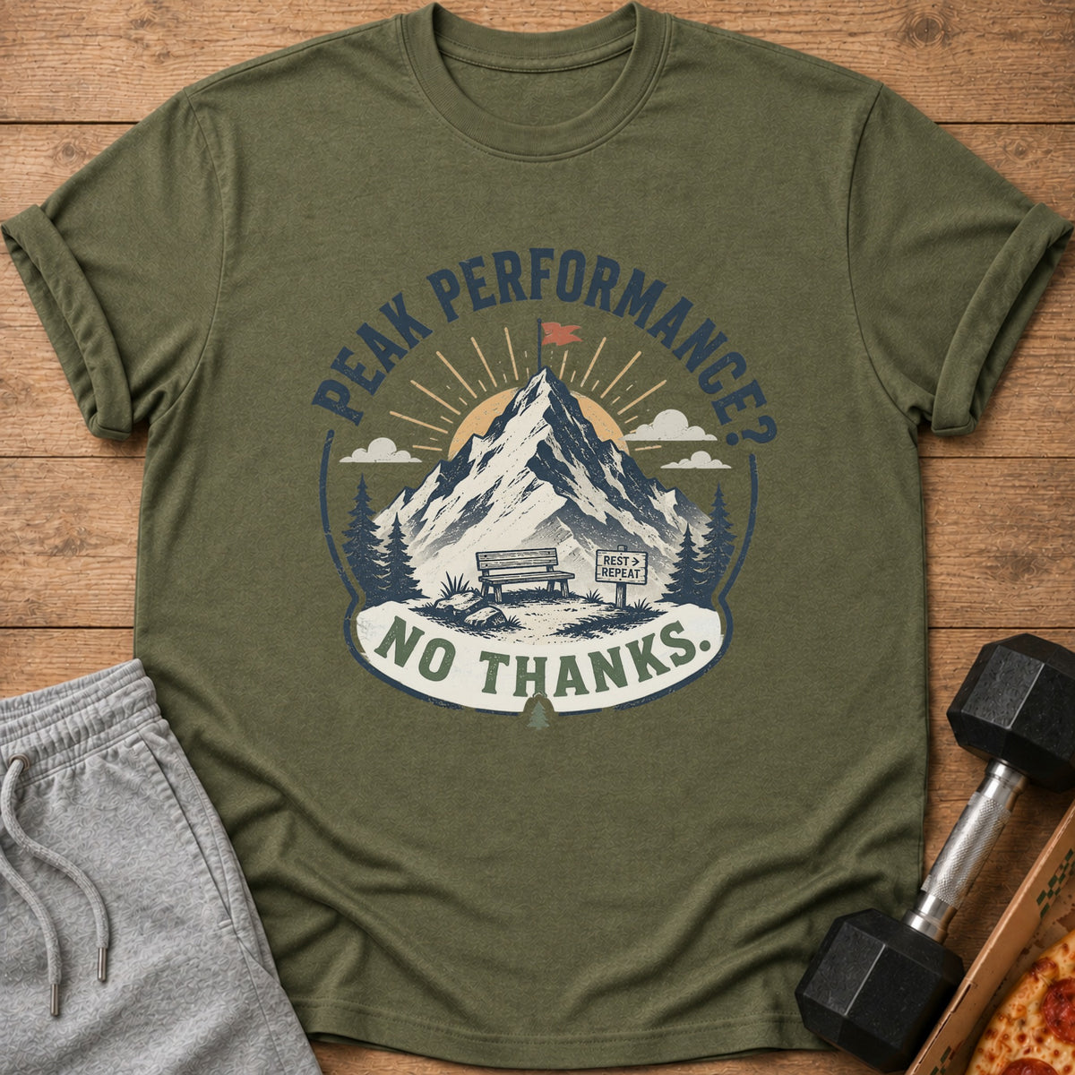 Olive green t-shirt with graphic of mountain, bench, and text "Peak Performance? No Thanks."