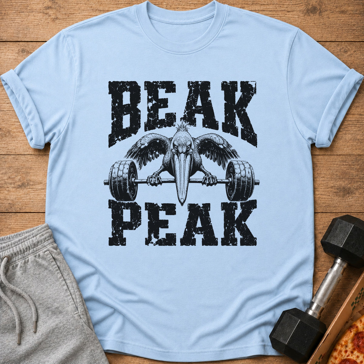 Light blue t-shirt with distressed black text "BEAK PEAK" and a pelican lifting a barbell.