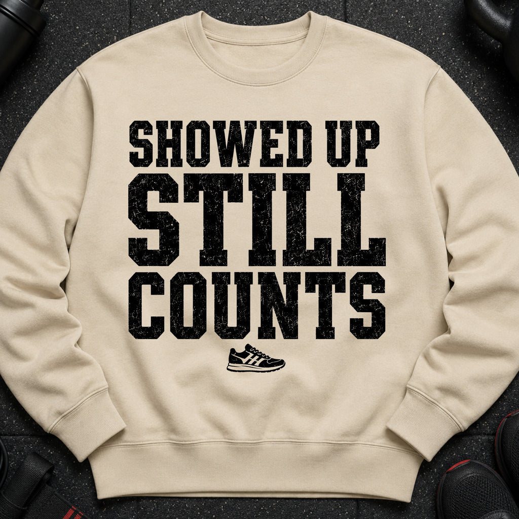 Light tan sweatshirt with black distressed text "SHOWED UP STILL COUNTS" and a sneaker graphic.