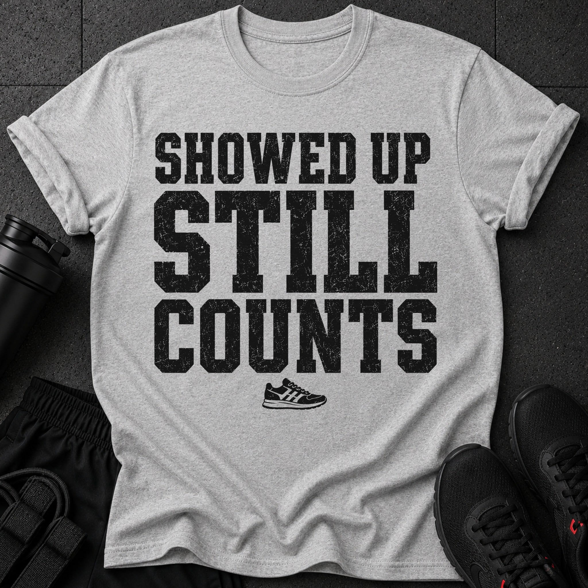 Gray t-shirt with distressed black text: "SHOWED UP STILL COUNTS" and a small sneaker graphic.