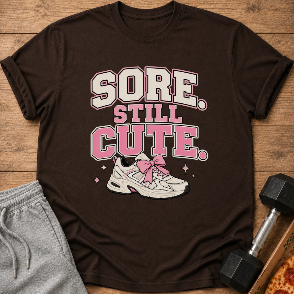 Brown t-shirt with text "SORE STILL CUTE" and a sneaker with a pink bow.