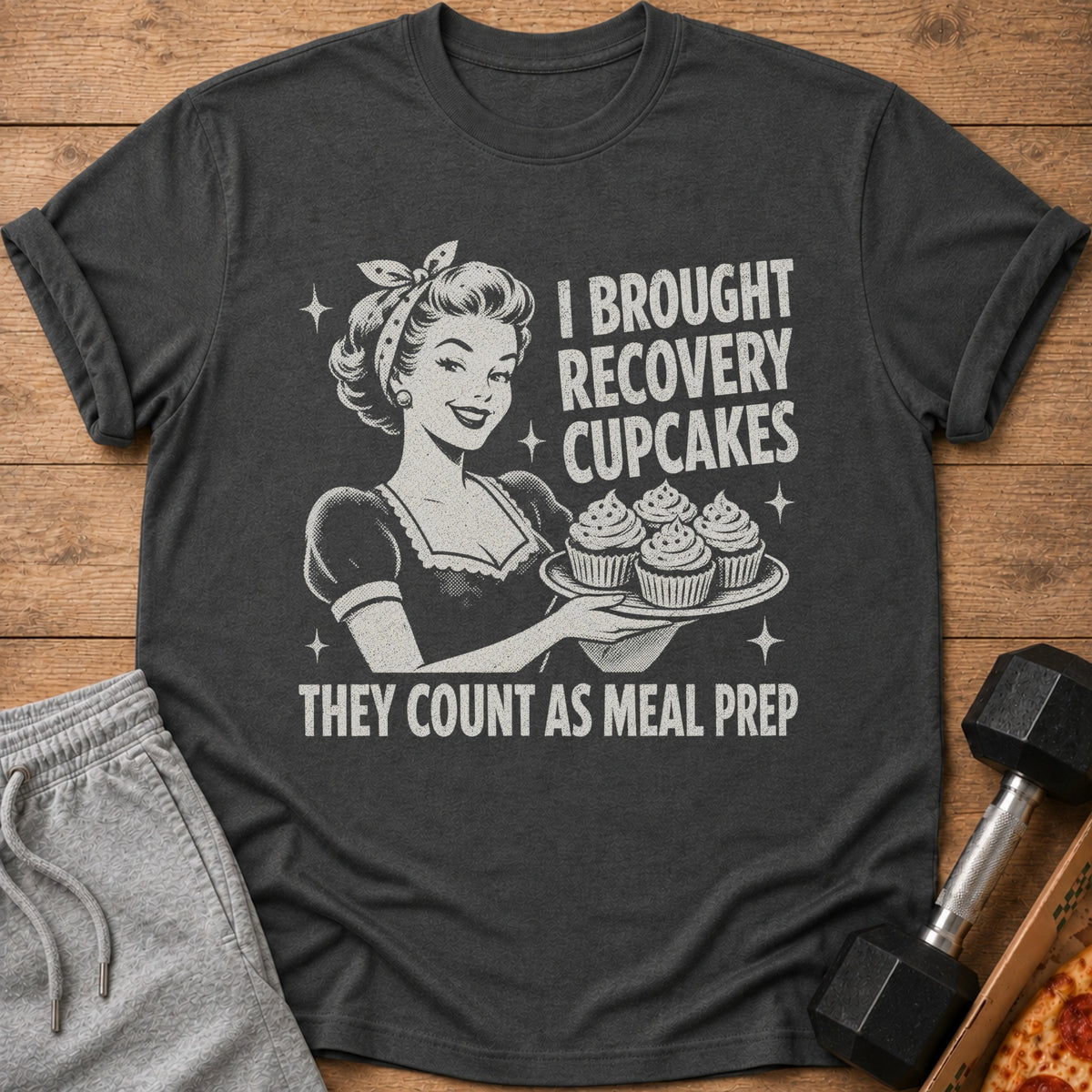 Dark t-shirt with retro woman holding cupcakes and text "I brought recovery cupcakes, they count as meal prep."