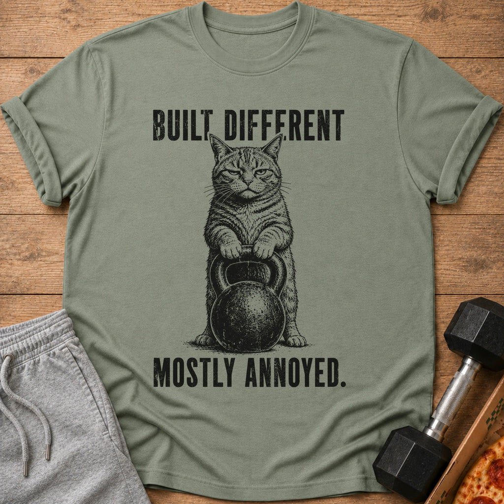 Green t-shirt with a cat holding a kettlebell and text "Built Different. Mostly Annoyed."