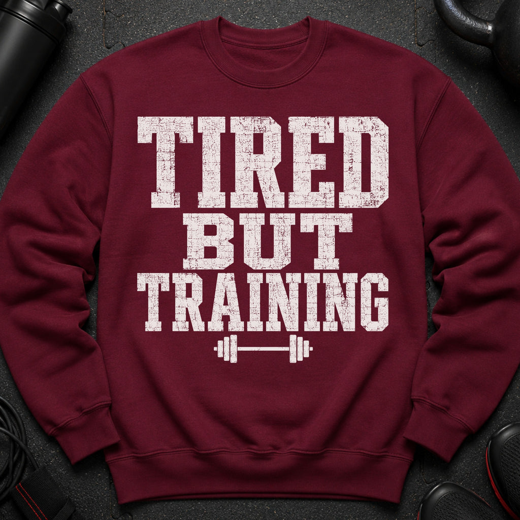 Maroon sweatshirt with white distressed text "TIRED BUT TRAINING" and a barbell graphic.