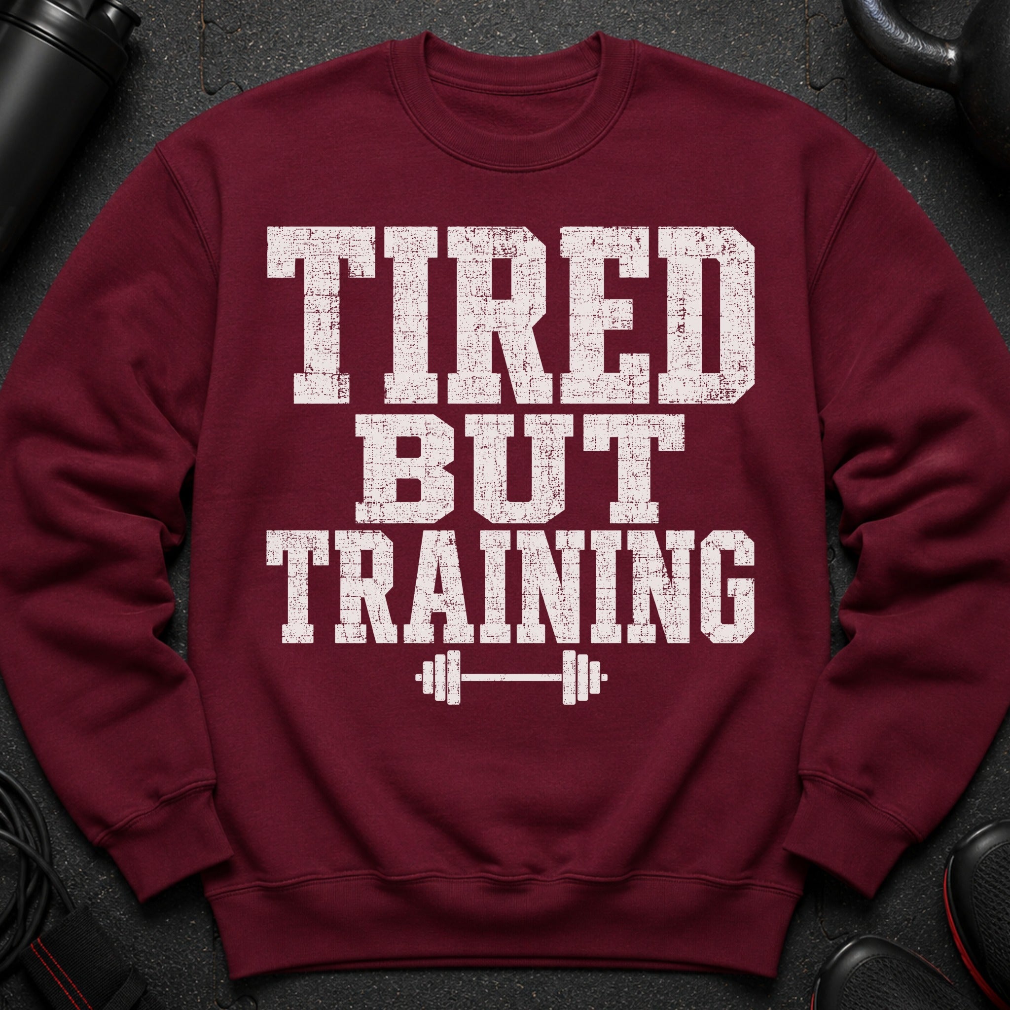 Maroon sweatshirt with white distressed text "TIRED BUT TRAINING" and a barbell graphic.