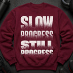 Maroon sweatshirt with white text "SLOW PROGRESS STILL PROGRESS".