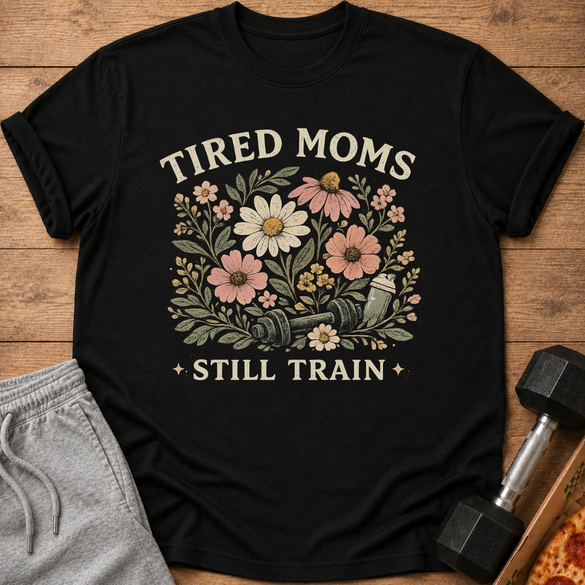 Black t-shirt with "Tired Moms Still Train" text and floral dumbbell graphic.